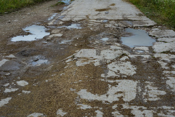 Old broken asphalt road with pits, puddles, mud, strewn with straw