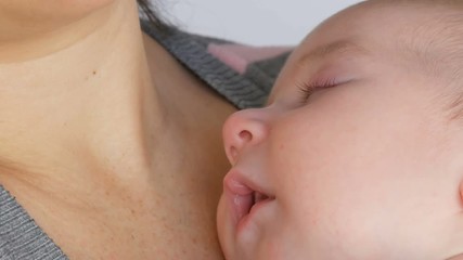 Young beautiful mother with long dark hair is holding a newborn infant baby of two months on a white background in studio
