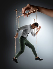 Hand of puppeteer manipulating man as marionette on grey background