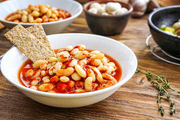 Tasty beans with tomato sauce in bowl on wooden table
