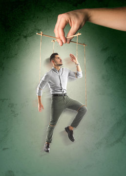 Hand of puppeteer manipulating man as marionette on color background