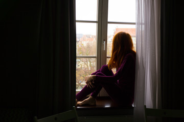 girl sitting on a windowsill and looking at the evening city