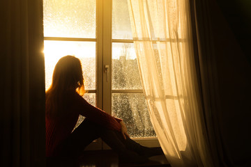 girl sitting on a windowsill and looking at the evening city