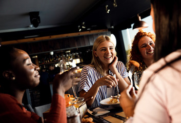 Group of young female friends having fun in restaurant, talking and laughing while dining at table.