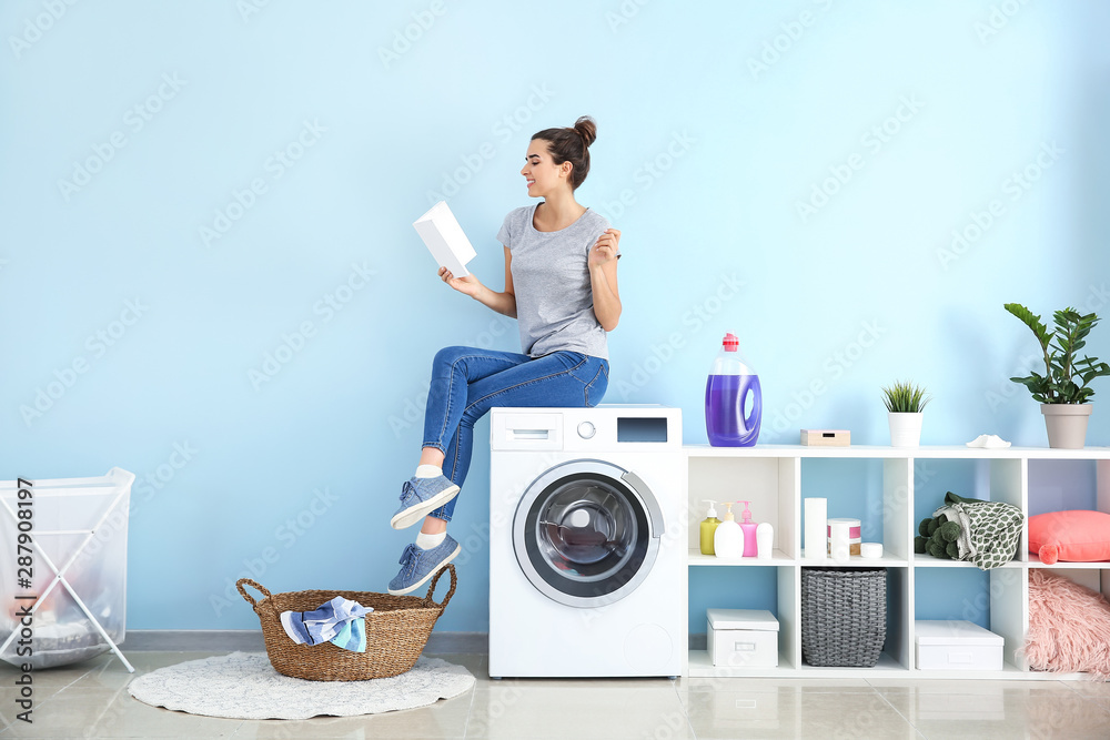 Wall mural beautiful young woman reading book while doing laundry at home