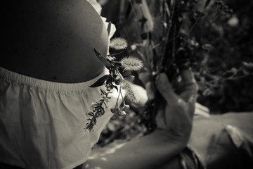 A small bouquet of meadow flowers in her hand on a bare shoulder in a white dress. Monochrome. Horizontal orientation.