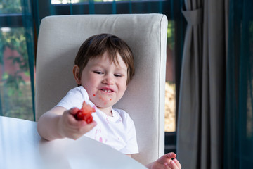 Cute boy eating fresh ripe strawberries at home