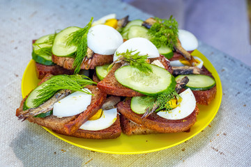 Sandwich from rye bread, sprats, cucumber, eggs, dill, etc.