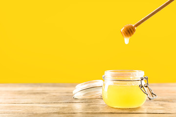 Jar and dipper with tasty honey on color background