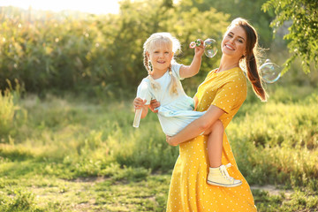 Happy mother and her little daughter blowing soap bubbles outdoors