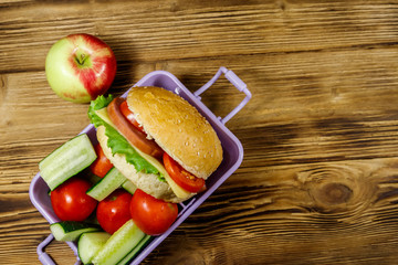 Apple and lunch box with burgers and fresh vegetables on a wooden table. Top view