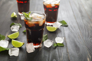 Glasses of cold cola, ice cubes and lime on wooden table