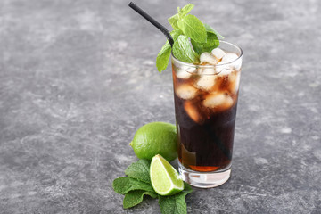 Glass of cold cola and lime on grey table