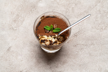 Portion of Classic tiramisu dessert in a glass cup on concrete background
