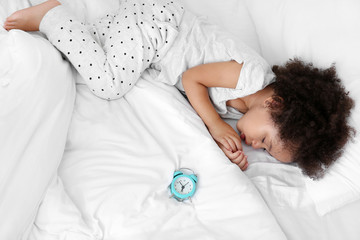 Obraz na płótnie Canvas Little African-American girl with alarm clock sleeping in bed