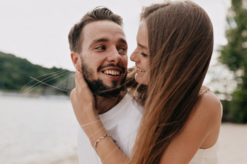 Beautiful young couple is talking and smiling while walking on the beach in sunny day. Man is looking at his girlfriend