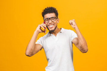 Happy winner. Portrait of a cheerful african american guy talking on mobile phone isolated against yellow background.