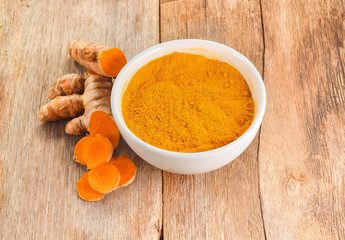 Turmeric roots with turmeric powder on wooden background