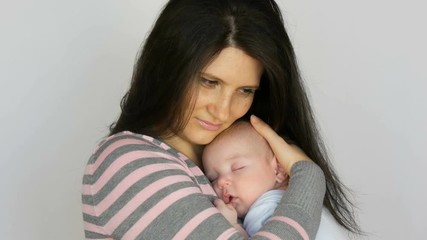 Young beautiful mother with long dark hair is holding a newborn infant baby of two months on a white background in studio
