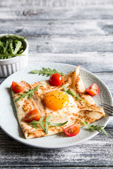 Crepes with eggs, cheese, arugula leaves and tomatoes. Galette complete. Traditional dish galette sarrasin.