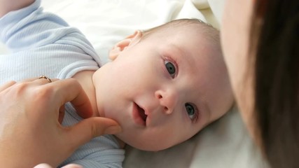 Mother gently touches and cradles her newborn baby in her arms while sitting on her bed. The child's face close up view