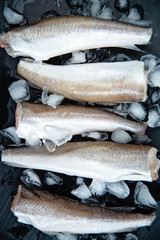 Raw fish hake. Five Raw fish fillet on ice on dark background,
