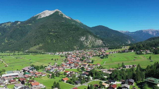 Aerial view of Tyrolean village Ehrwald surrounded by mountains during summer, lush green hills and clear blue sky - landscape panorama of Alps from above, Germany/Austria border, Europe