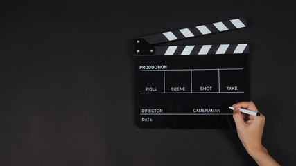 Fototapeta na wymiar Black Clapperboard or clap board or movie slate with right hand holding pen use in video production ,film, cinema industry on black background.