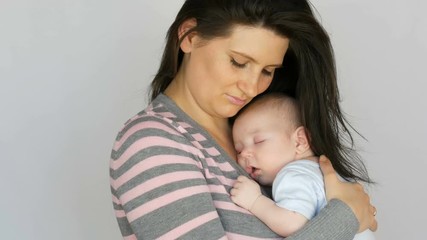 Young beautiful mother with long dark hair is holding a newborn infant baby of two months on a white background in studio