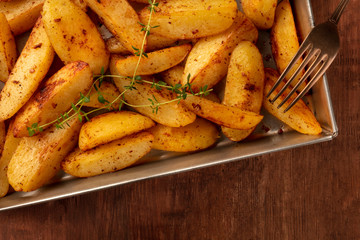 Potato wedges, oven baked with thyme, close-up overhead shot in a baking tray on a dark rustic wooden background with a place for text