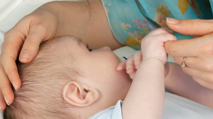 Mother gently touches and cradles her newborn baby in her arms while sitting on her bed. The child's face close up view