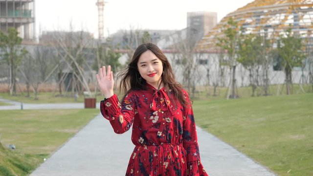 Portrait of a beautiful Chinese girl in red dress turning round and waving her hand to say goodbye to her friend, 4k footage, slow motion.