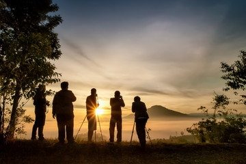 Mountain view morning silhouette a group of Photographers standing on top hill with yellow sun...