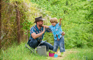 Naklejka na ściany i meble Personal example. Spring garden. Little helper in garden. Planting flowers. Growing plants. Take care of plants. Boy and father in nature with watering can. Dad teaching little son care plants
