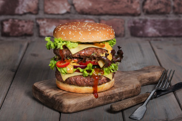 Hamburger with a double serving of meat, tomatoes, salad, onions on a wooden board in a restaurant.Copy space