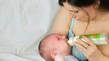 A two-month newborn baby lies on the mother arms and sucks a nipple from a bottle of milk.