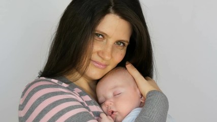 Young beautiful mother with long dark hair is holding a newborn infant baby of two months on a white background in studio