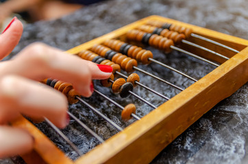 A woman's hand with red nail Polish counts on wooden bills that lie on a marble table close-up