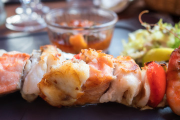 Roasted pieces of white and red fish fillet on a skewer with garnish, sauce and salad, close up, Mediterranean style