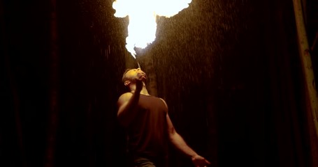 man is creating fire from his mouth during amazing fire show in darkness outdoors