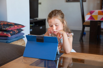 portrait of four years old blonde cute girl, in living room of home, watching digital tablet on table 