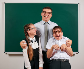 Portrait of a teacher, schoolboy and schoolgirl with old fashioned eyeglasses posing on blackboard background - back to school and education concept