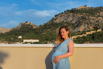 Fototapeta na wymiar Profile view of pregnant woman with long hair in blue sky dress outdoor