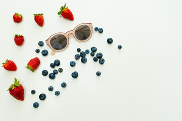 Summer flat lay composition with fresh berries and sunglasses in center.