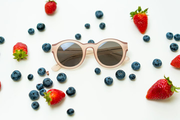 Strawberries, blueberries and pink sunglasses flat lay background.