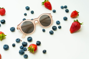 Summer flat lay background with pink sunglasses and different berries around.