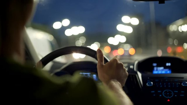 Man drives a car in the night city and listen music. Black view