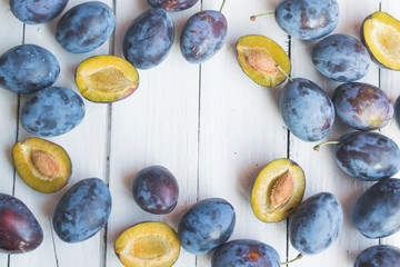 Fresh and ripped delicious plums on old white wooden table making a frame