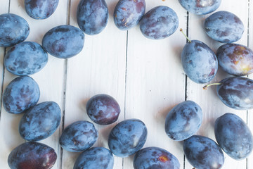 Fresh and ripped delicious plums on old white wooden table making a frame