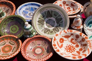 set of original bright handmade ceramic clay plates and toy bells, handpainted with floral and abstract patterns enjoy direct sunshine, Ukrainian traditional folklore symbolic art, Podillya style